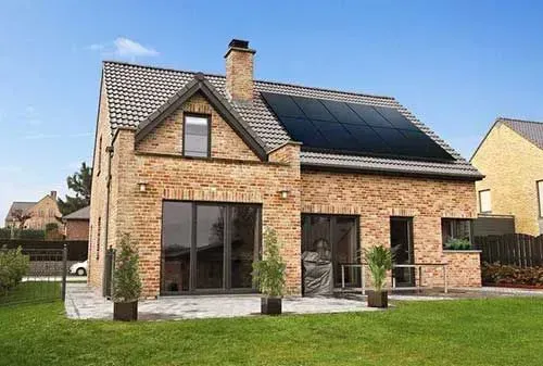 Brick house with large solar panels, sliding glass doors, and a green lawn under a blue sky