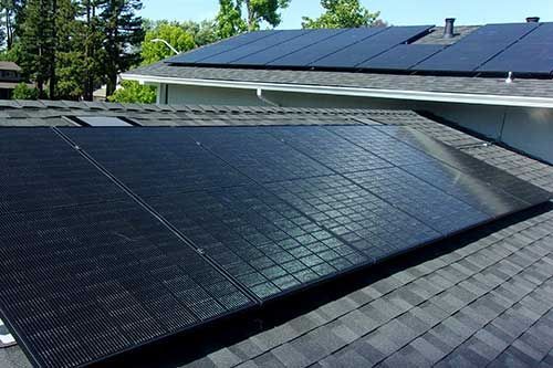 Black rooftop solar panels on a sloped shingle roof in daylight