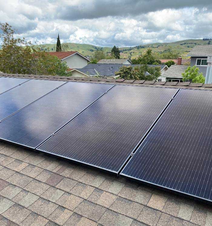 Solar panels installed on a shingled rooftop with hills and cloudy sky in the background