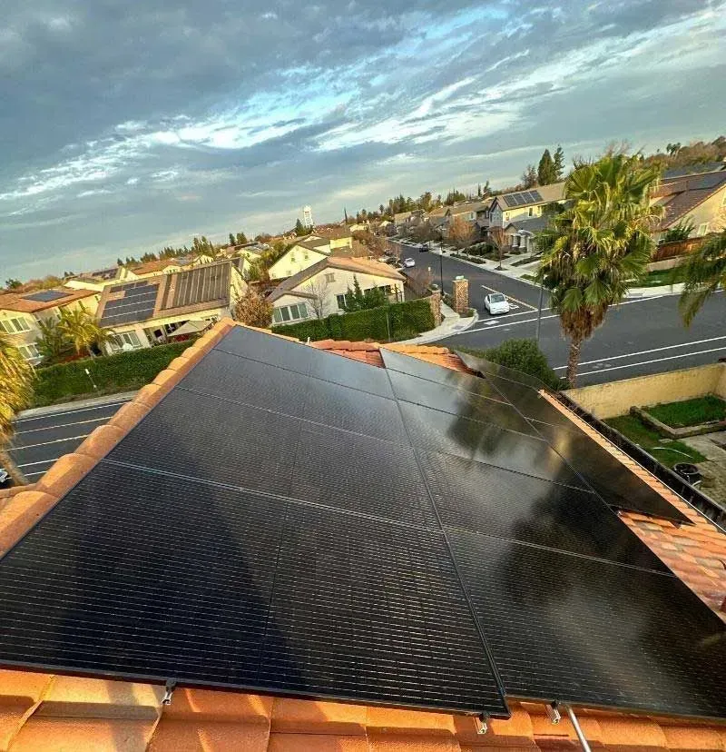 Solar panels on a rooftop overlooking a suburban neighborhood at sunset