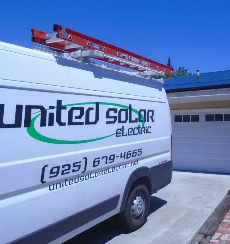 White United Solar Electric van with red ladder parked in a driveway beside a garage.