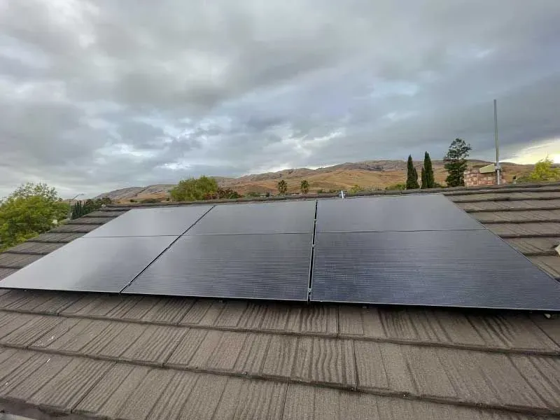 Solar panels on a rooftop with cloudy sky and hills in the background