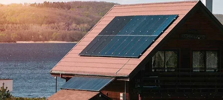 House with blue solar panels on a lakeside at sunset