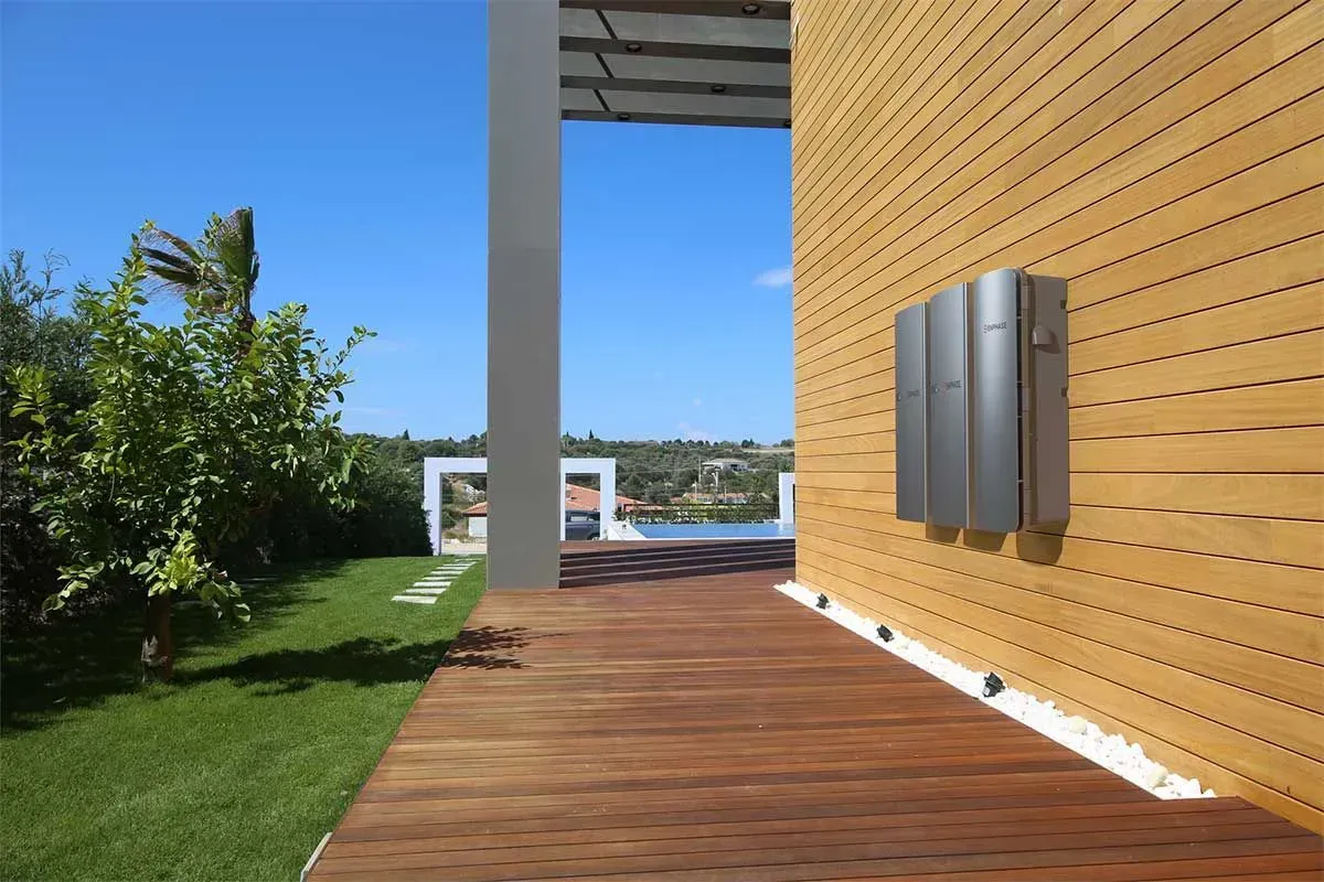 Modern patio with wooden deck, green lawn, yellow wall, and view of the water under a blue sky