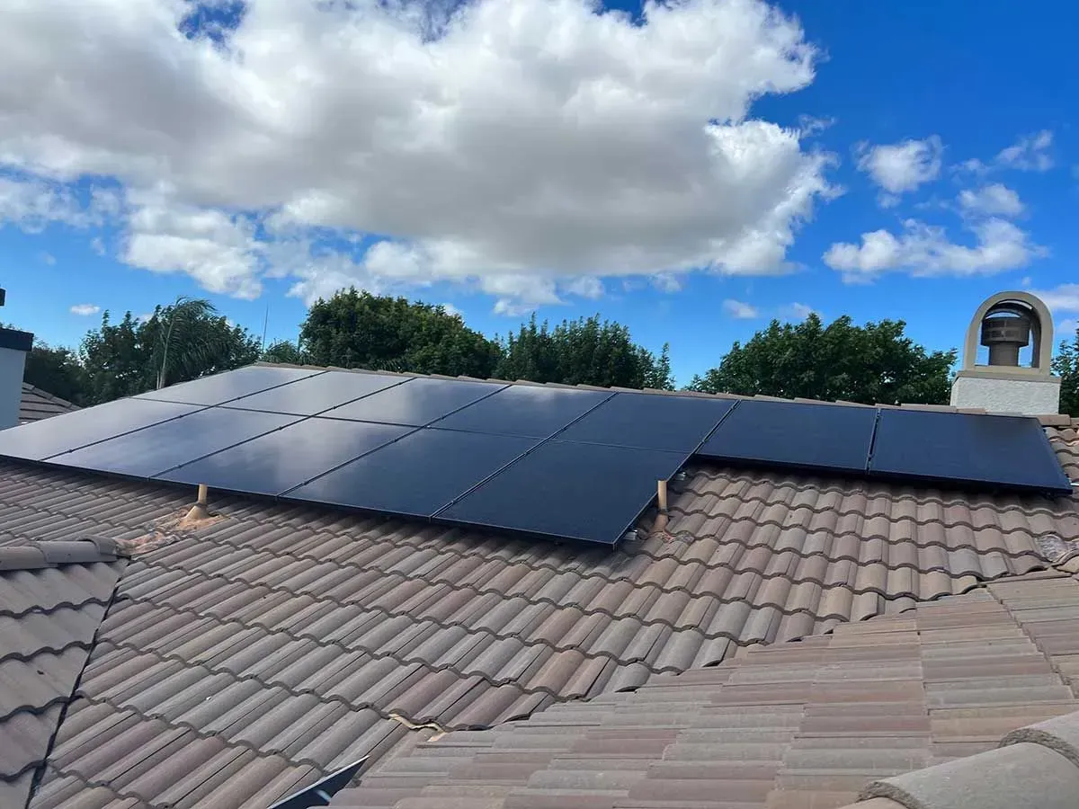 Solar panels mounted on a tiled rooftop under a partly cloudy sky