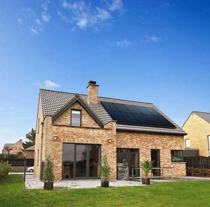Brick house with solar panels and large windows on a grassy lawn under a blue sky