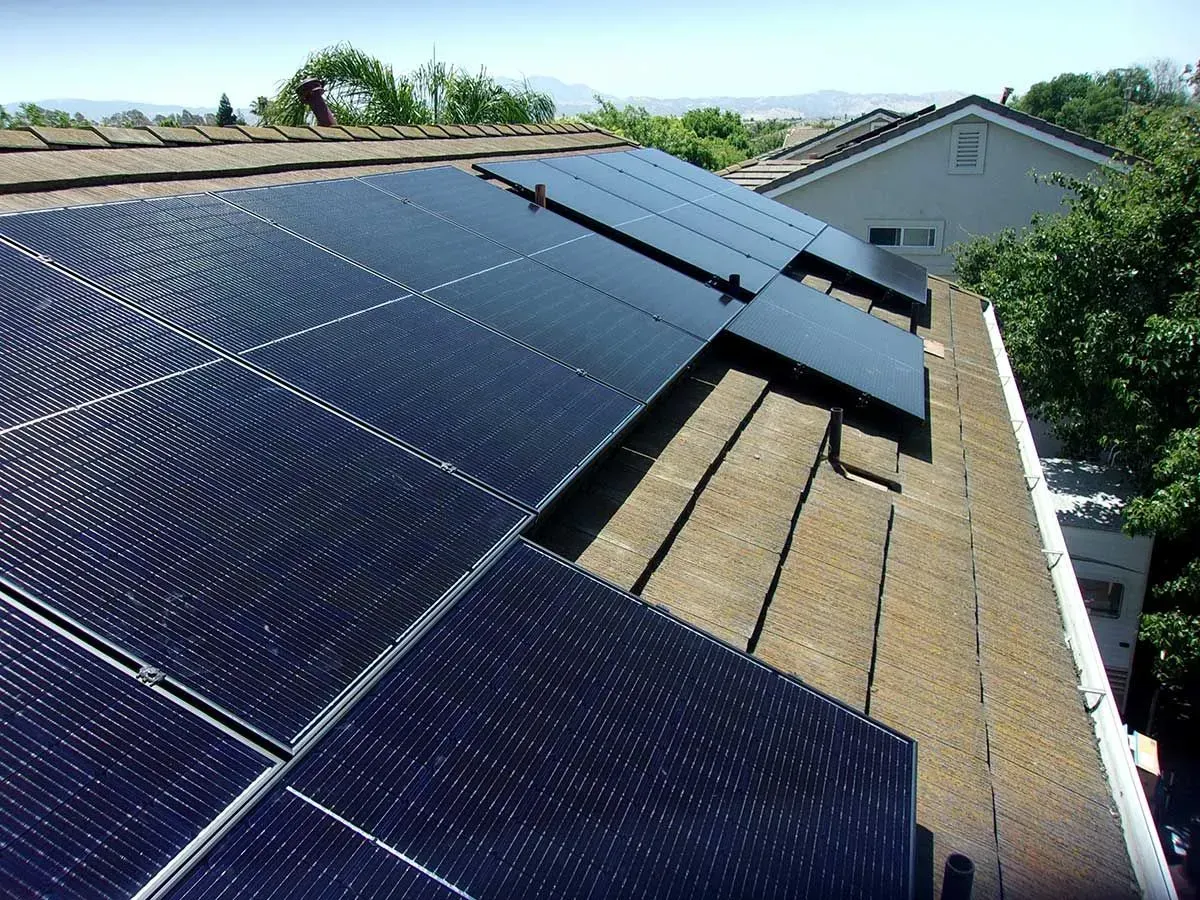 Solar panels installed on a rooftop beside a neighboring house under a clear sky