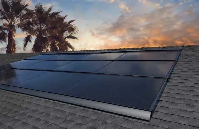 Solar panels on a shingled roof at sunset, with palm trees in the background
