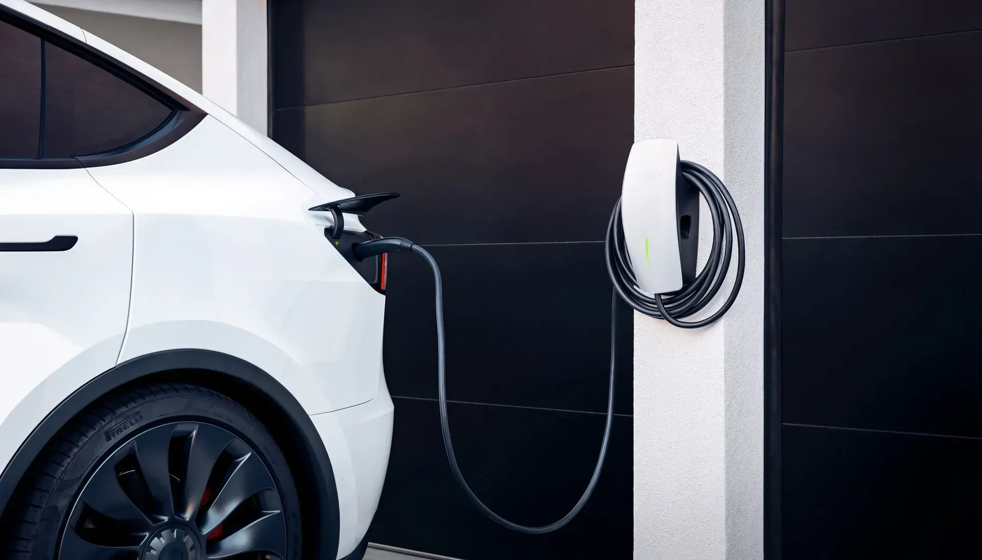 White electric car charging at a wall-mounted station in a garage or parking area.