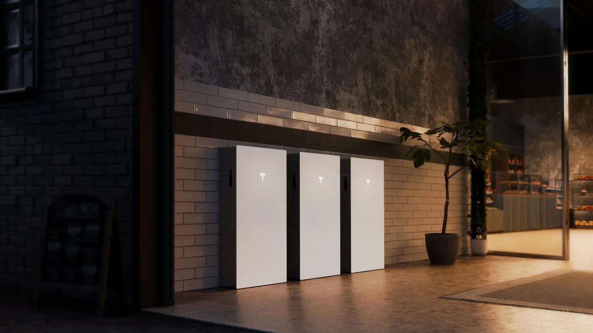 Three white charging kiosks against a dark wall in a modern indoor lobby, with a potted plant nearby.