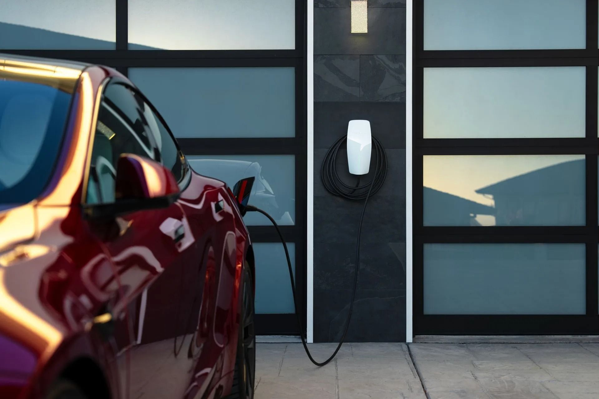 Red electric car plugged into a home charging station in a garage