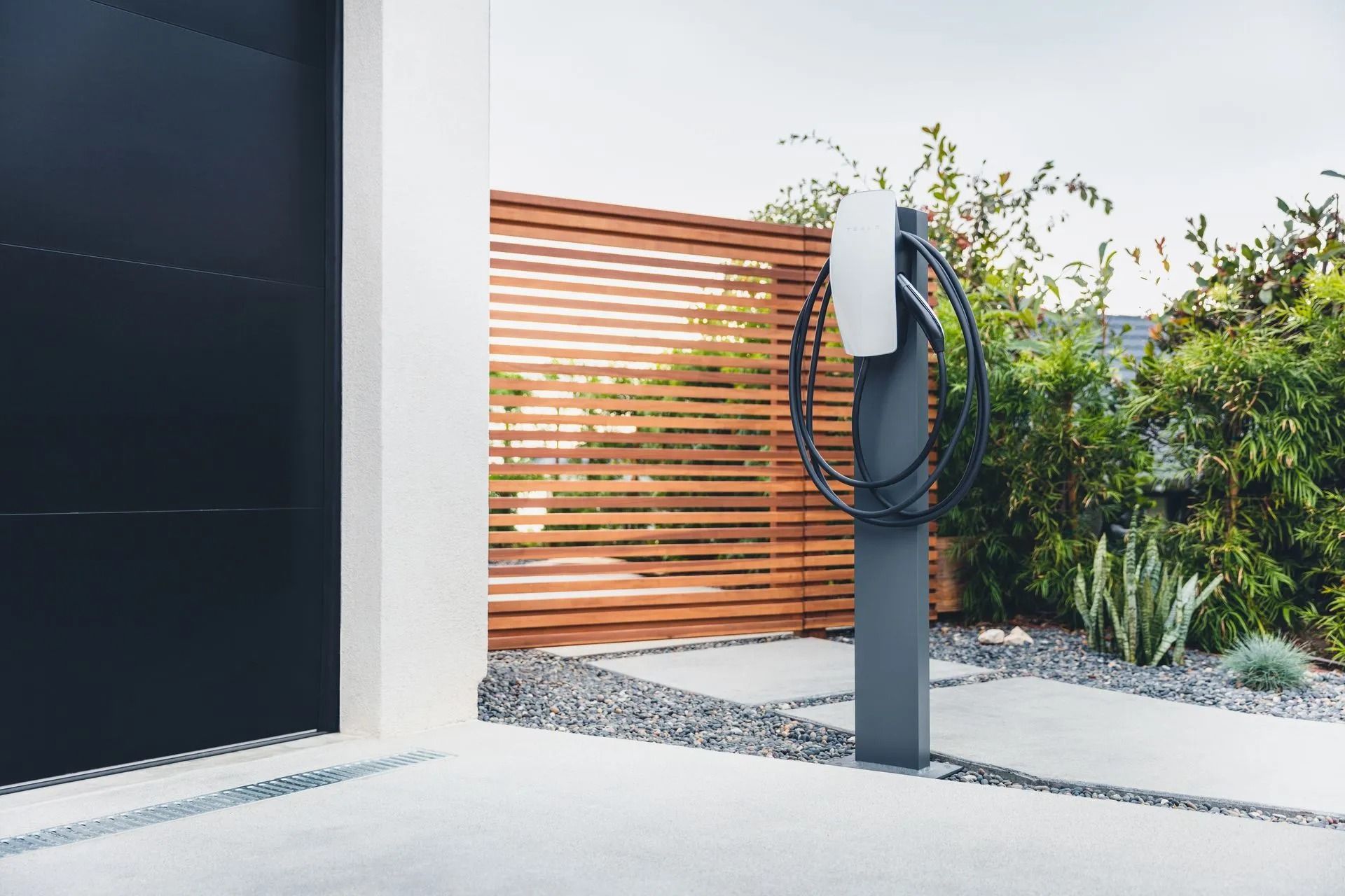 Outdoor EV charging station beside a modern home, with a black charger on a post and wood fence backdrop