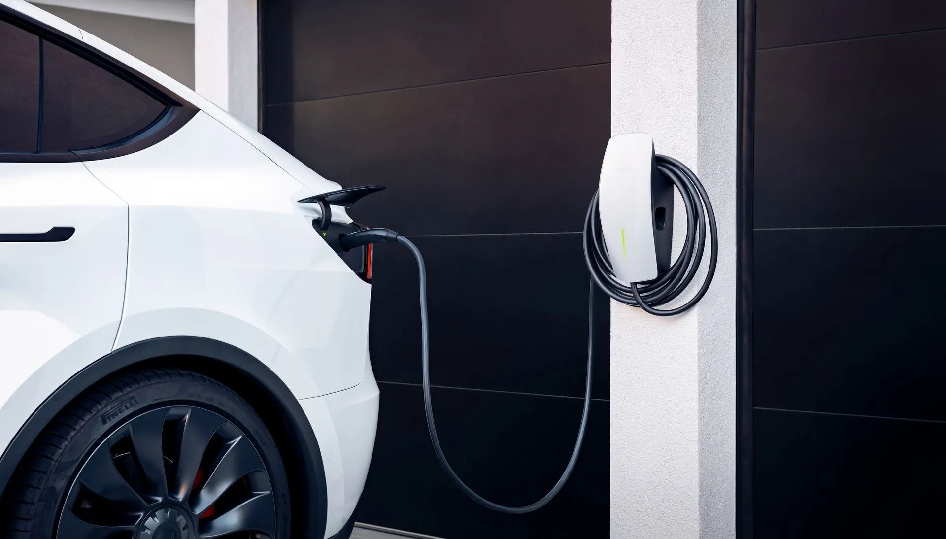 White electric car charging at a wall-mounted station in a garage