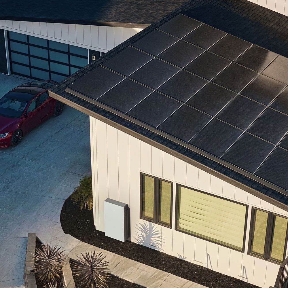 Aerial view of a solar-paneled roof beside a red car in a driveway.
