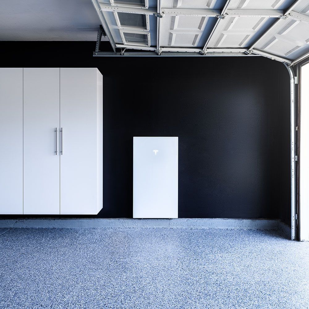 Empty garage with black wall, white cabinets, and a small white freezer on a gravel floor.