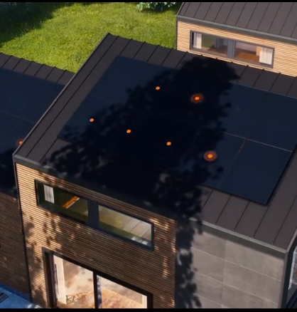 Aerial view of a modern dark-roofed house with multiple skylights and nearby greenery.
