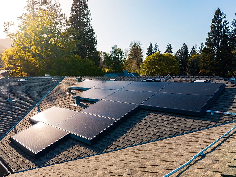 Solar panels installed on a shingled rooftop at sunset, with trees in the background.