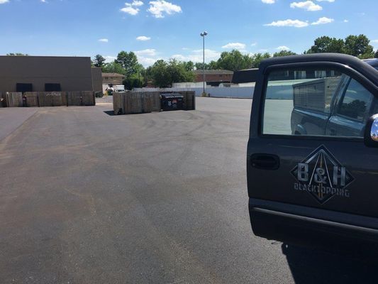A parked gray pickup truck with open door on asphalt; a business logo, a sunny day.