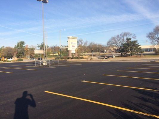 Empty parking lot with yellow lines under a clear blue sky. Shadow of person holding camera.