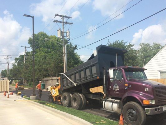 Asphalt paving: Dump truck unloading onto paving machine on a street, workers nearby.