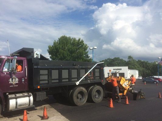 Truck unloading asphalt for paving; workers with equipment on a parking lot under a cloudy sky.