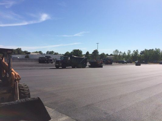 Asphalt paving with dump trucks and a tractor on a sunny day.