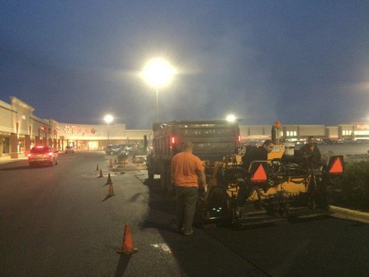 Asphalt paving crew at work in a commercial parking lot at dusk.