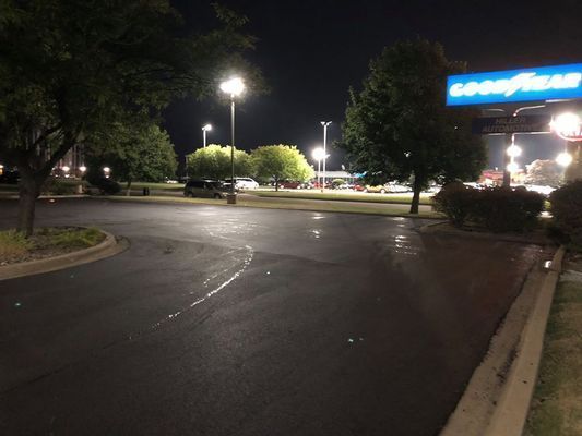 Dark asphalt parking lot at night, lit by streetlights. Goodyear sign visible.