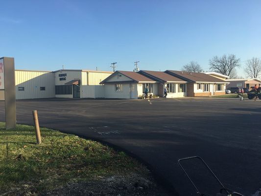 A building with a dark paved lot in front. Sunny day, light brown roofs, beige walls.