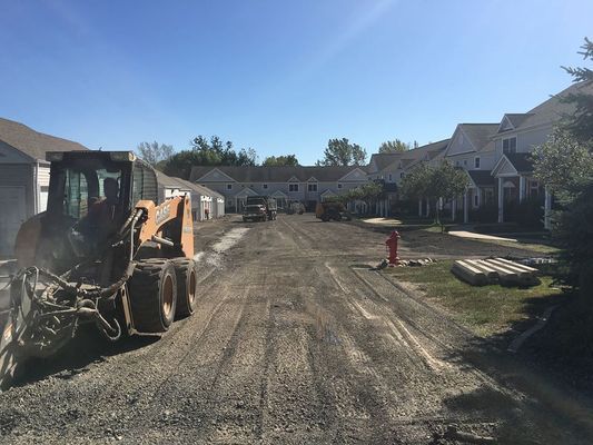 A construction site with a loader in the foreground, preparing a road in front of townhouses.