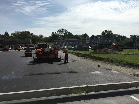 Asphalt paving in progress: crew laying black asphalt in a parking lot on a sunny day.