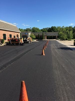 Freshly paved asphalt parking lot with orange traffic cones and construction equipment.