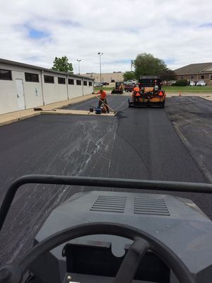Asphalt paving: Workers lay new asphalt with a roller machine, in a parking lot setting.