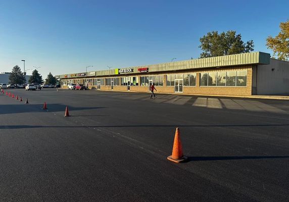 A strip mall with orange cones in the parking lot; a person walks by.