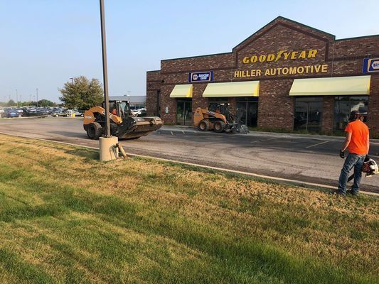 Construction work outside of a Goodyear Hiller Automotive store; skid steers and a worker with a saw are present.
