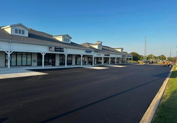A newly paved commercial strip mall with storefronts and a clear blue sky.