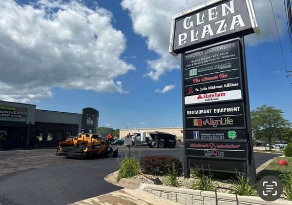 Glen Plaza sign with businesses listed, asphalt paving in progress.