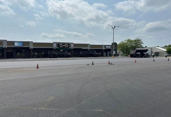 An empty parking lot with orange cones in front of a strip mall on a cloudy day.