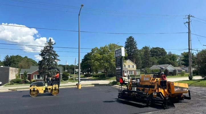 Asphalt paving in progress on a sunny day. A roller and paver work on the black surface.