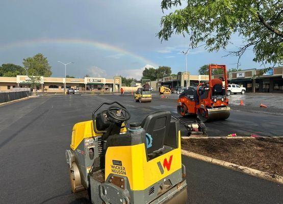 Asphalt paving of a parking lot with construction equipment, including rollers and a rainbow overhead.