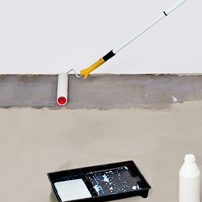 A paint roller is being used to waterproof a basement floor.