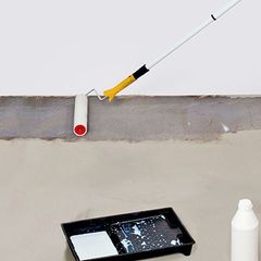 A paint roller is being used to waterproof a basement floor.