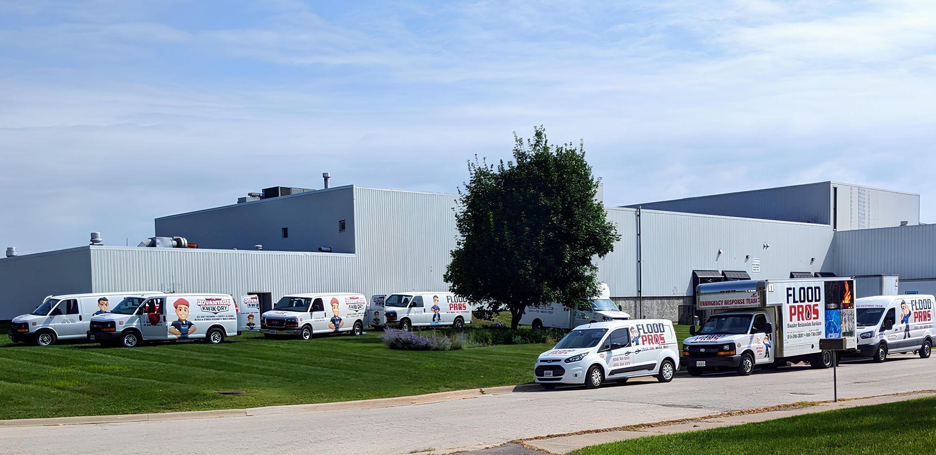 White service vans parked in front of a large gray industrial building on a sunny day.