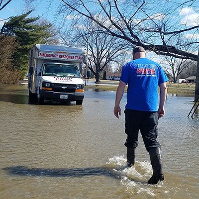 Man in boots walks through flood towards an emergency response van.