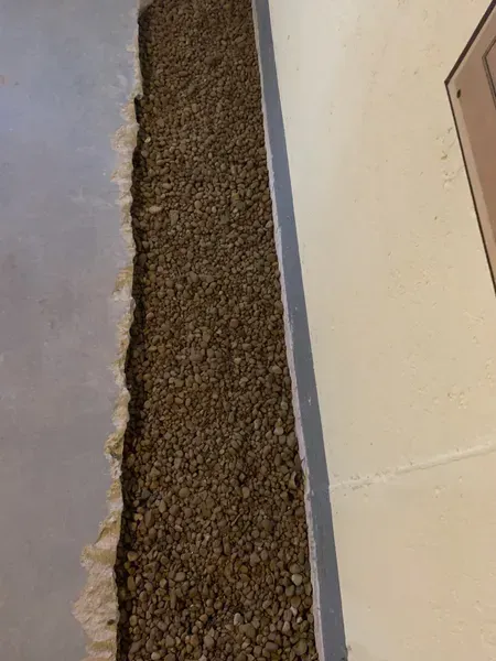A pile of gravel is sitting on the floor next to a wall.