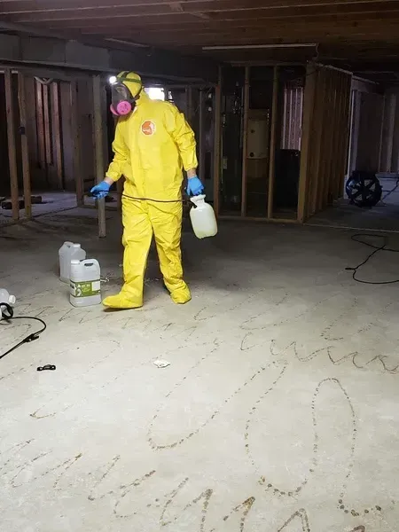 A man in a yellow suit is spraying something on the floor.