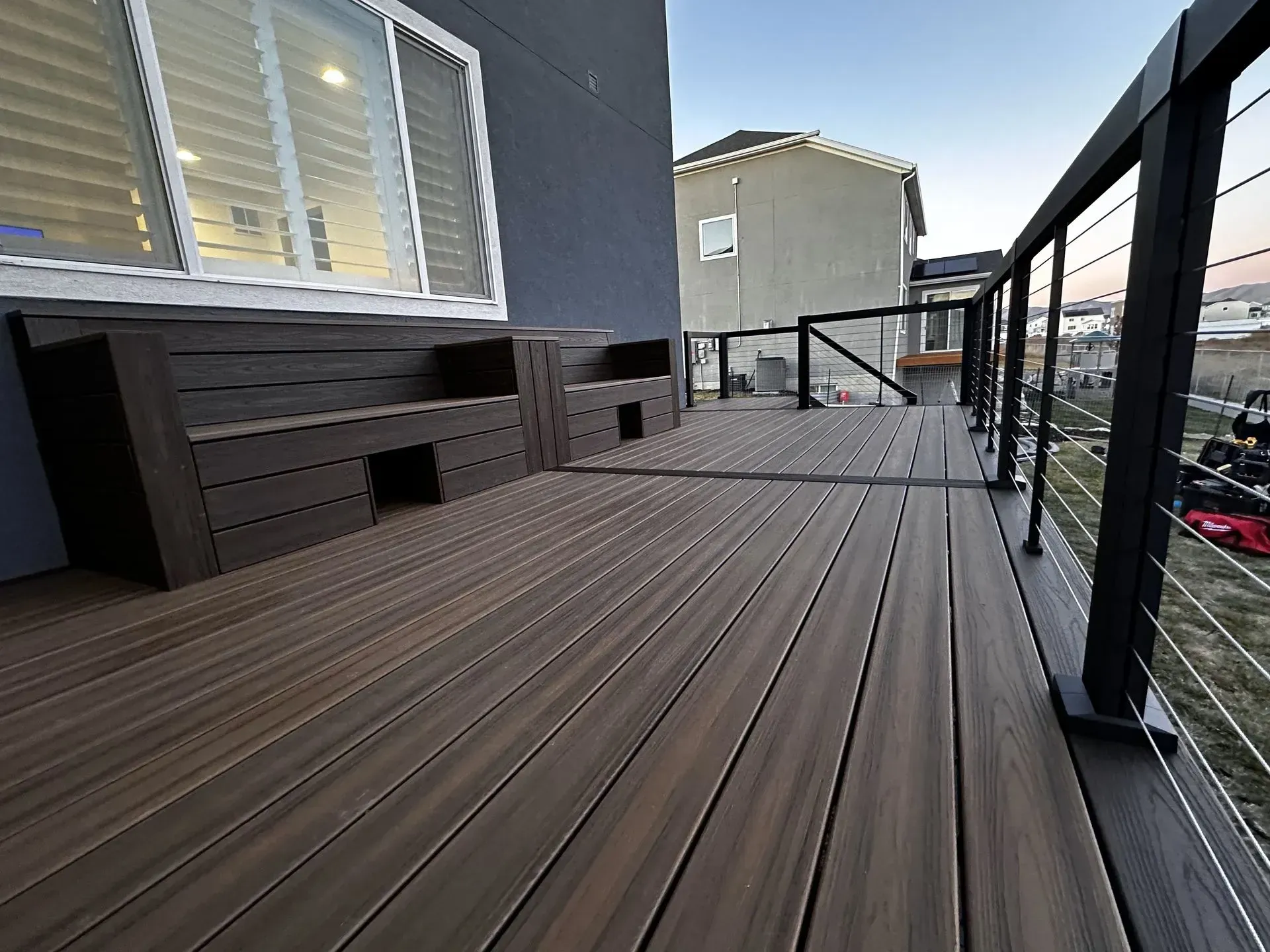 A brown composite deck with black railing and built-in bench, overlooking a neighborhood.