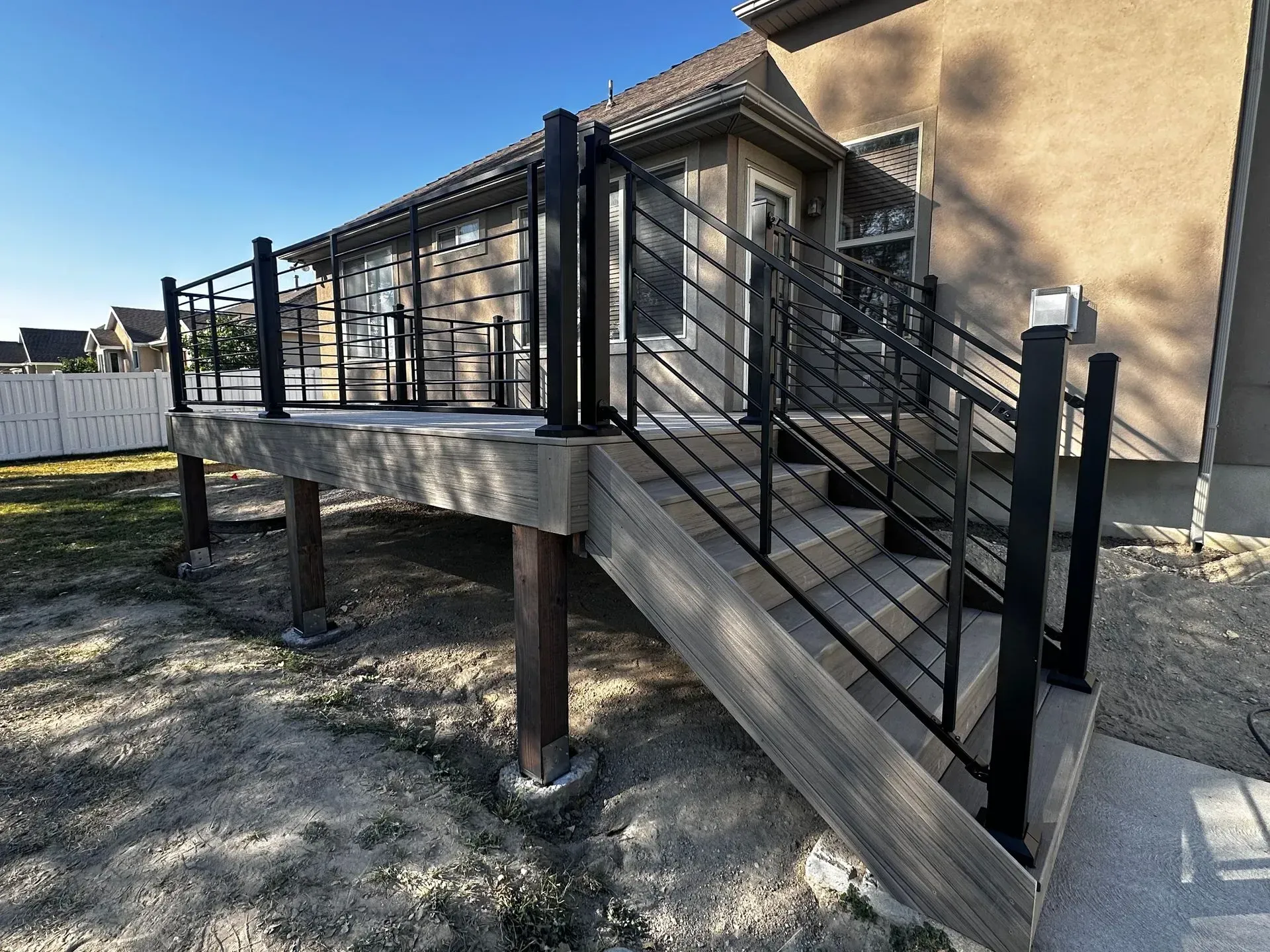Wooden deck with black metal railings and stairs. Adjacent to a house with tan siding.