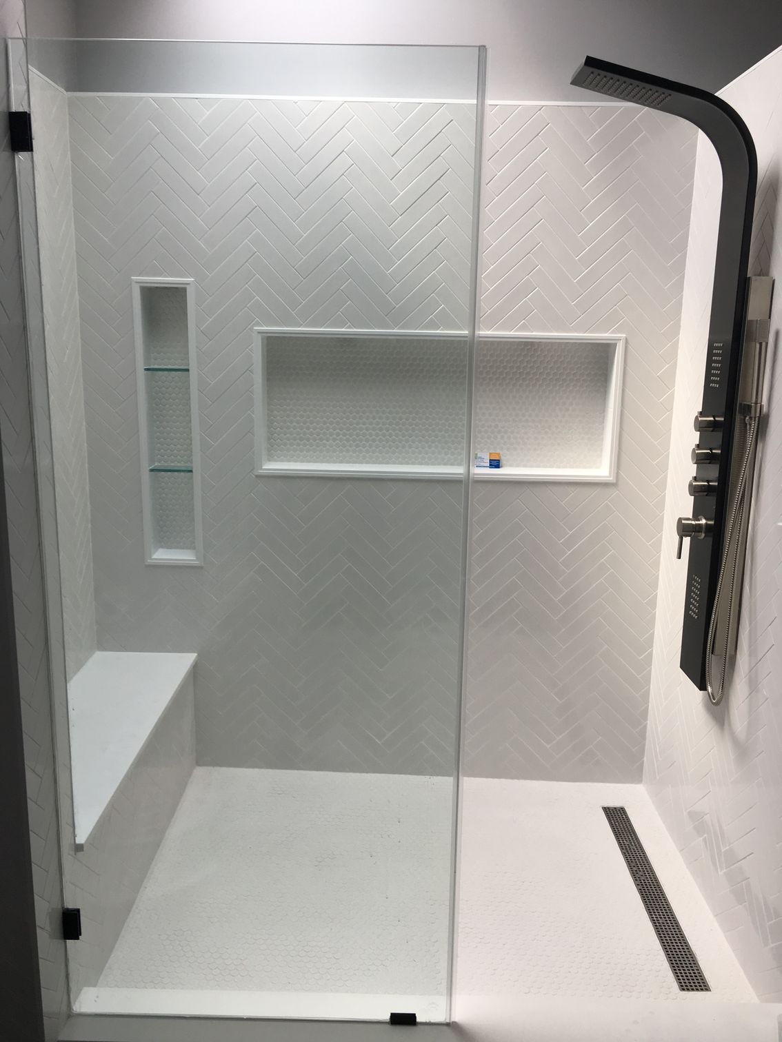 A walk in shower with a glass door and a bench.