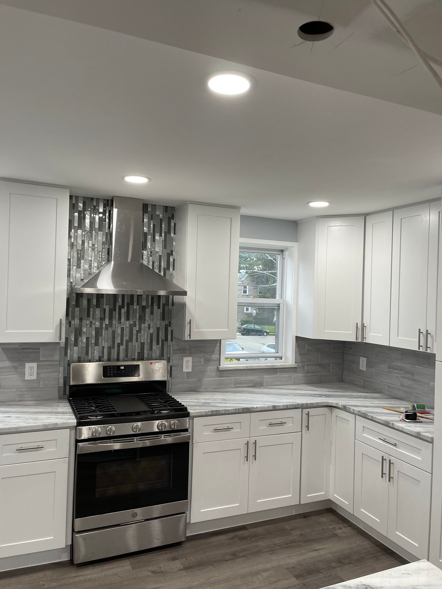 A kitchen with white cabinets , a stove , and a window.